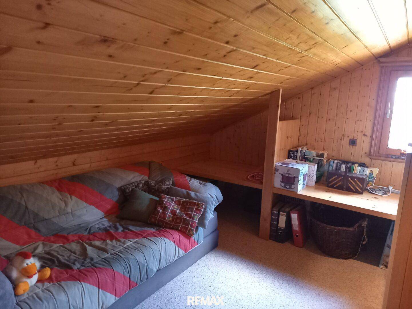 Dachgeschosszimmer mit Holzverkleidung, Schlafsofa und integriertem Schreibtisch für flexible Nutzung.