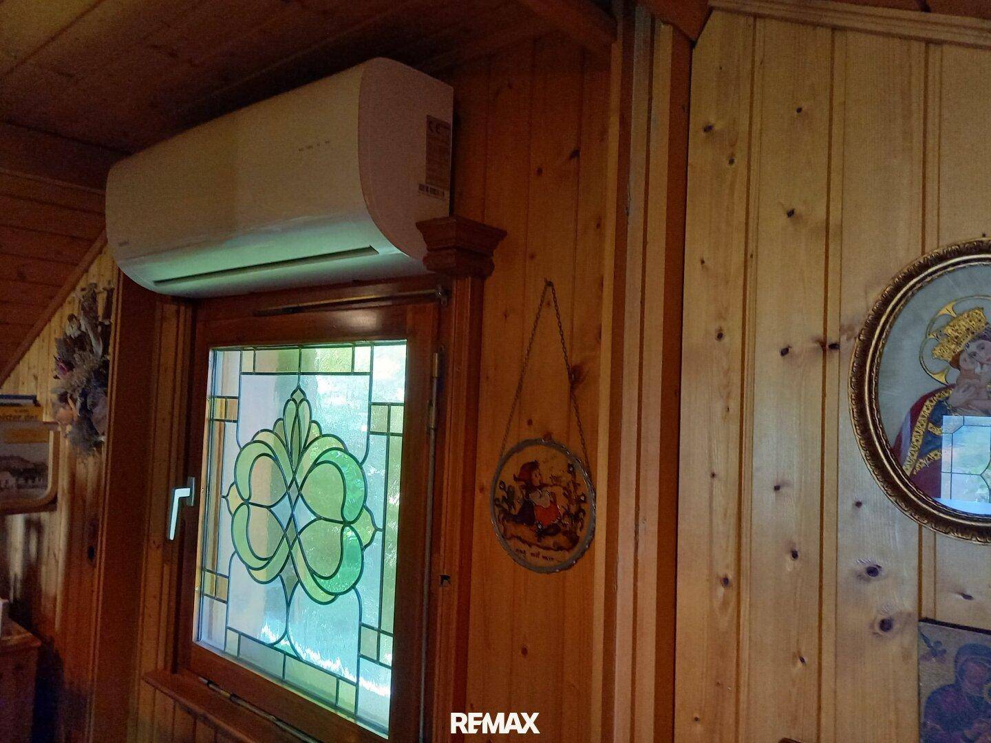 Fenster mit Buntglas und Klimaanlage in einem holzvertäfelten Raum mit traditioneller Dekoration.