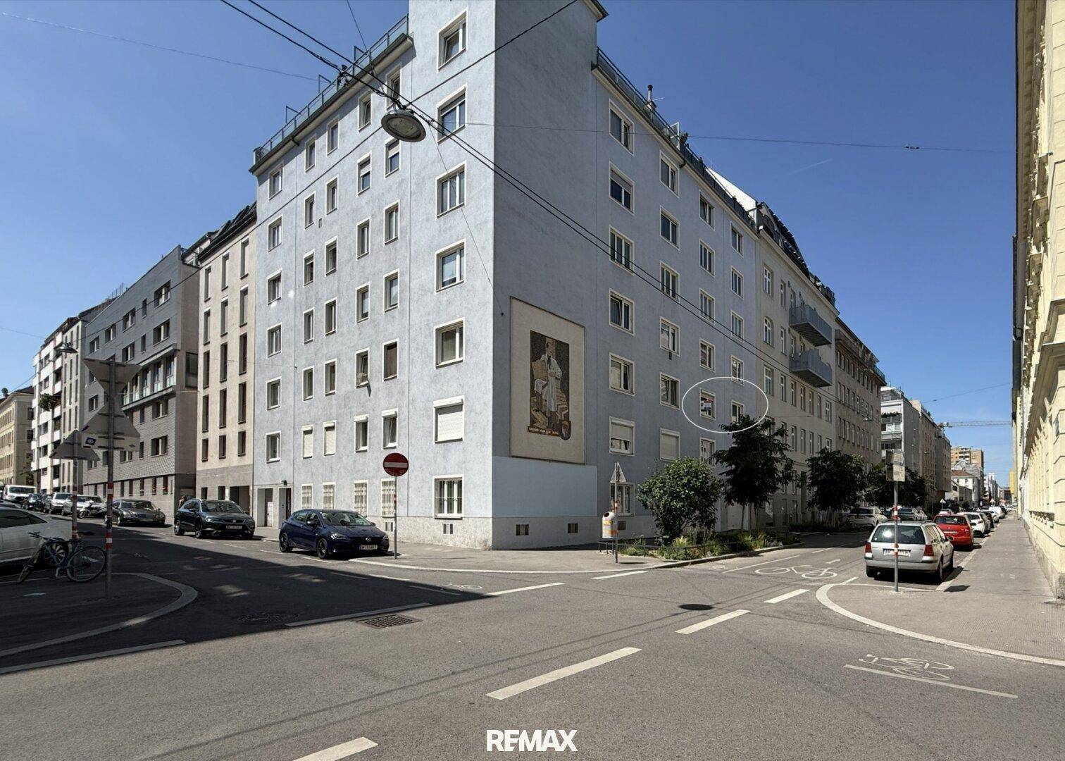 Außenansicht eines Mehrfamilienhauses an einer Straßenecke unter blauem Himmel.