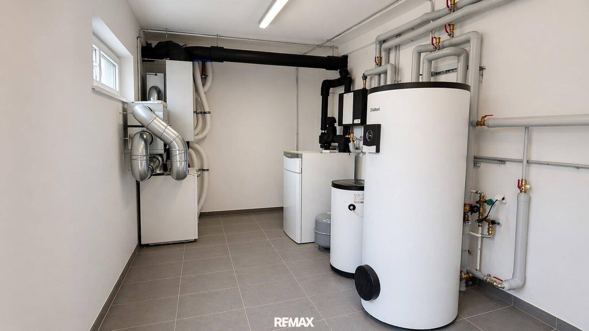 Technikraum mit moderner Heizungsanlage, Warmwasserspeichern und sauber gefliestem Boden.