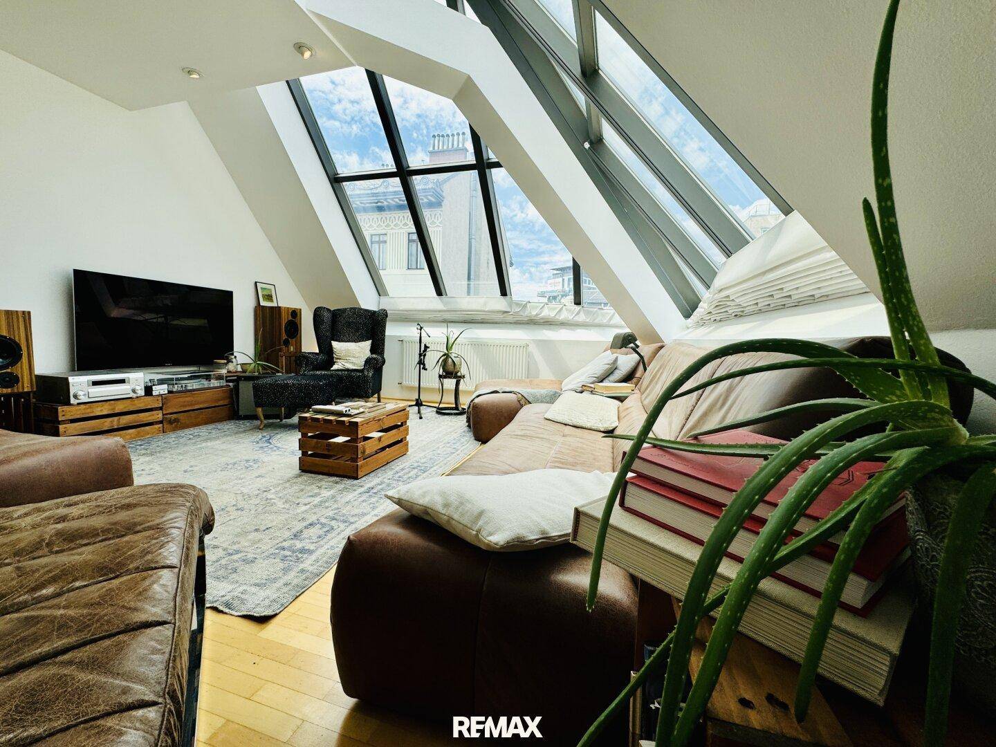 Wohnzimmer mit Fernseher, Audiosystem und bequemen Sitzgelegenheiten unter den Dachfenstern.