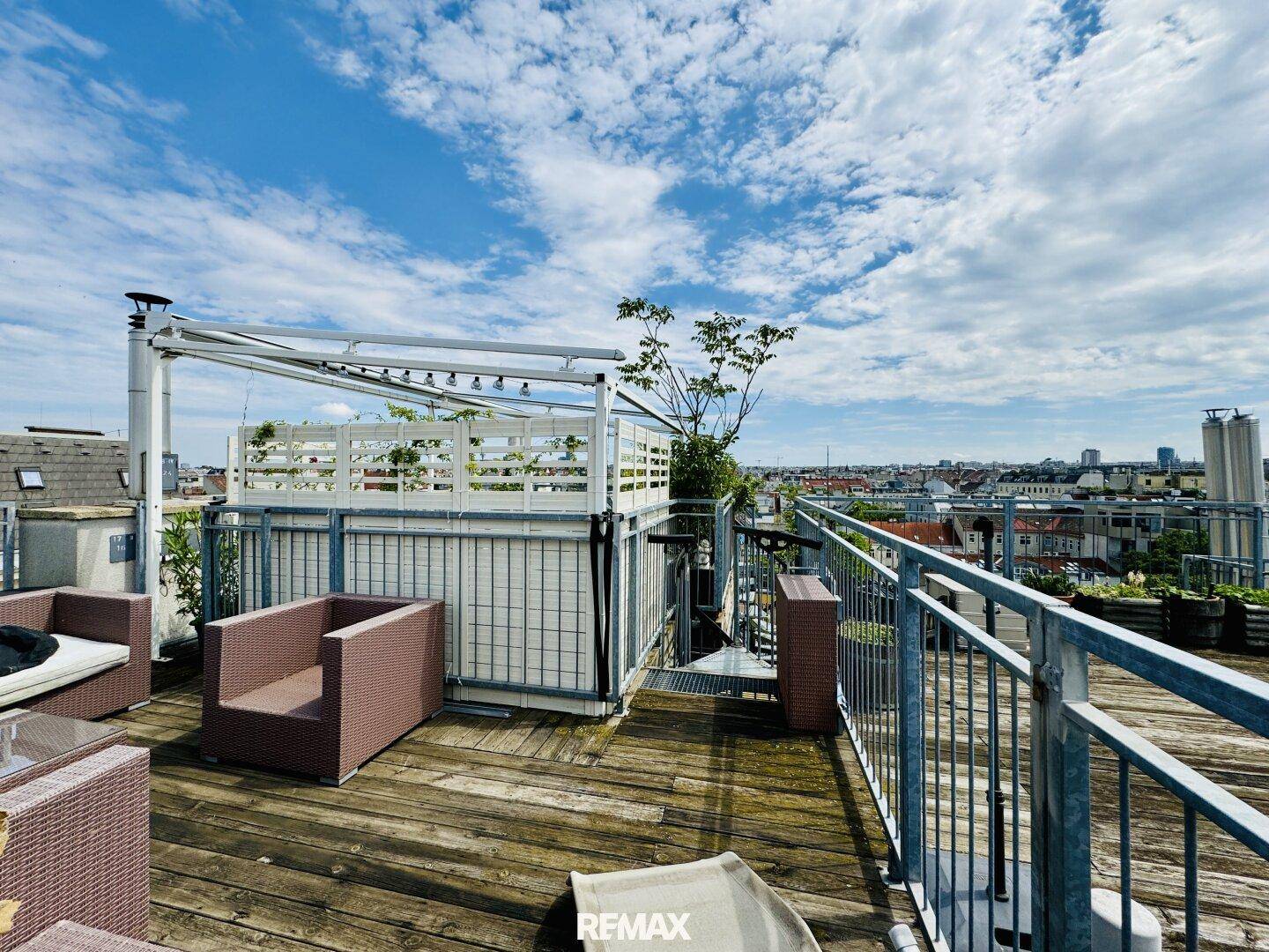 Weitläufige Dachterrasse mit Holzboden, Pflanzen und Blick auf die umliegenden Dächer.