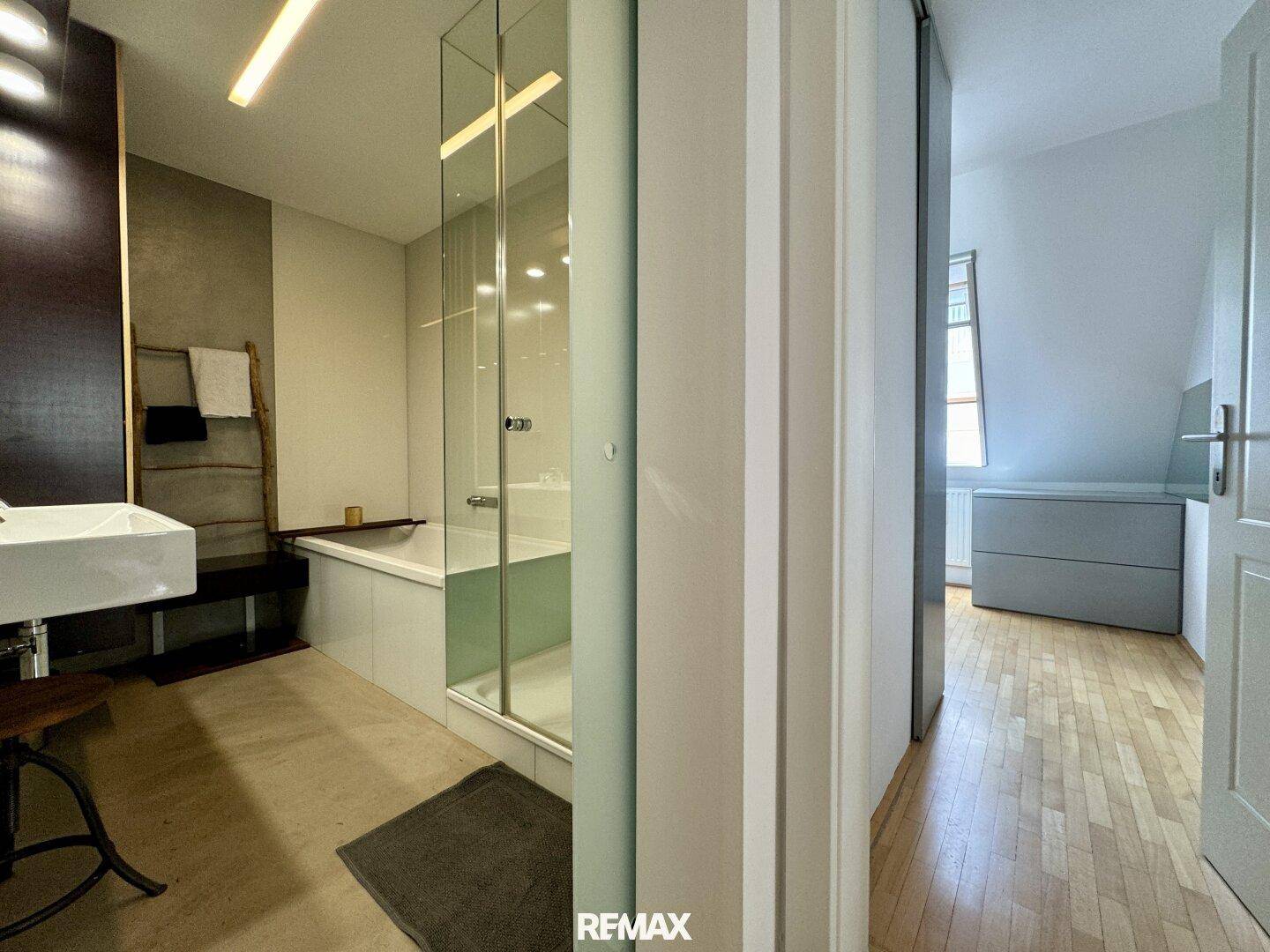 Modernes Badezimmer mit Badewanne, Glasdusche und Zugang zu einem Schlafzimmer.