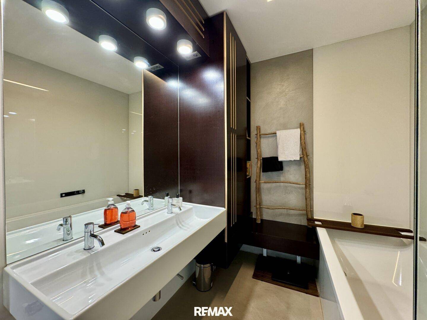Elegantes Badezimmer mit großem Doppelwaschbecken, Spiegel und moderner Beleuchtung.