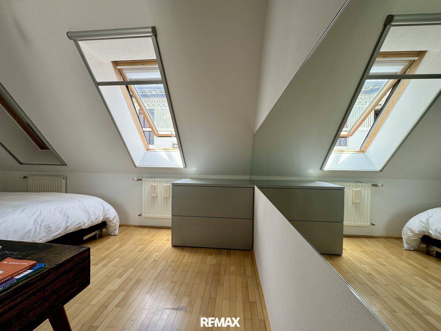 Helles Schlafzimmer mit Holzboden, Dachfenstern und einem großen Spiegel.