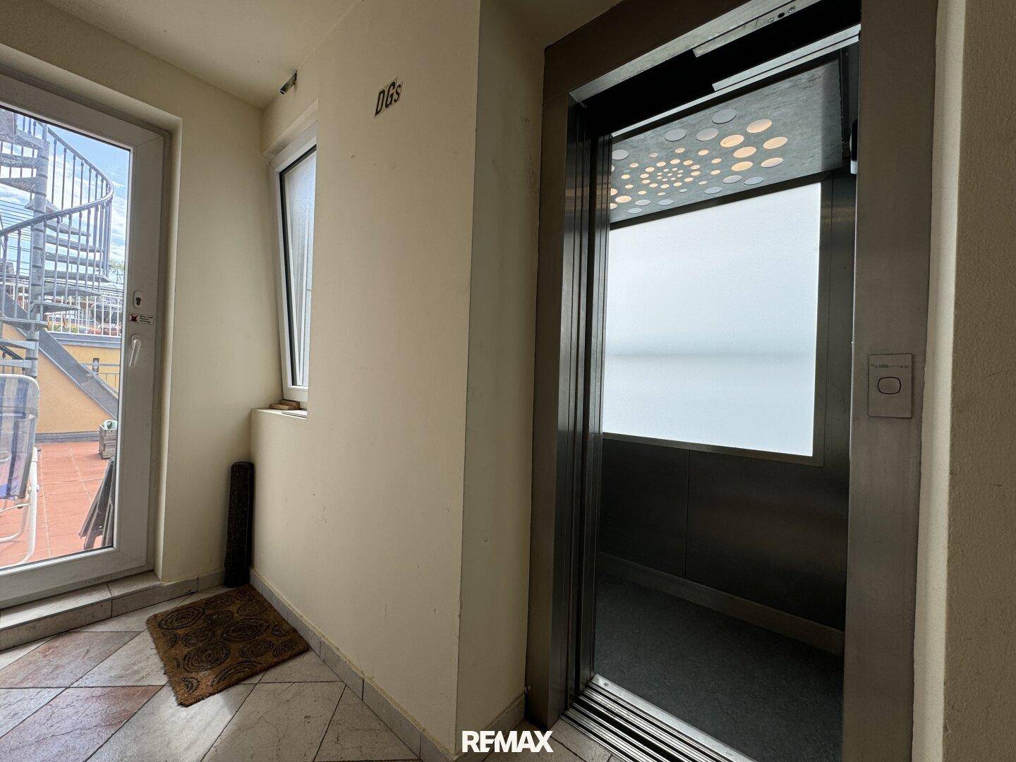 Heller Flur mit Aufzug und Zugang zu einer Außentreppe, die zur Dachterrasse führt.