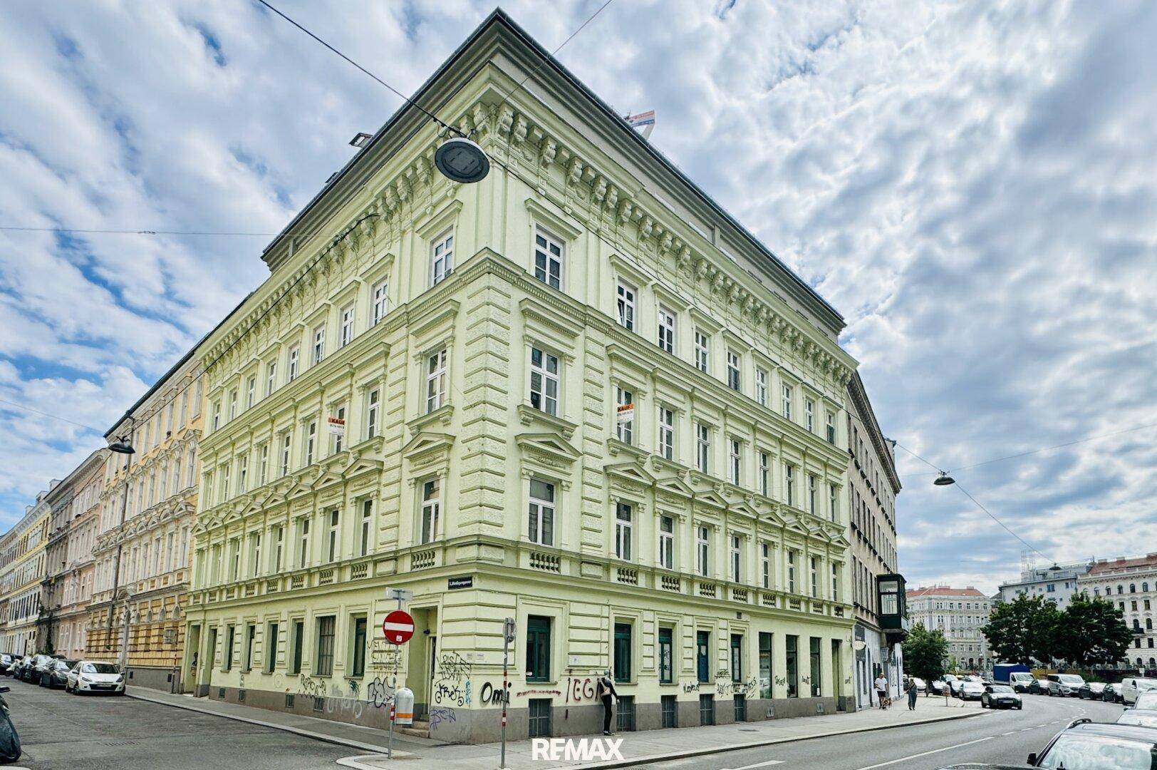 Historisches Eckgebäude mit klassischer Architektur und vielen Fenstern in urbaner Umgebung.