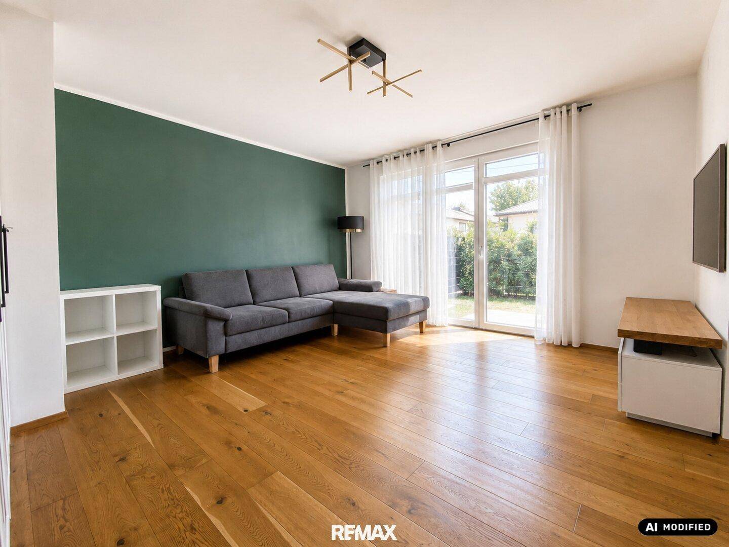Geräumiges Wohnzimmer mit Holzboden, grüner Akzentwand und Zugang zum Garten.