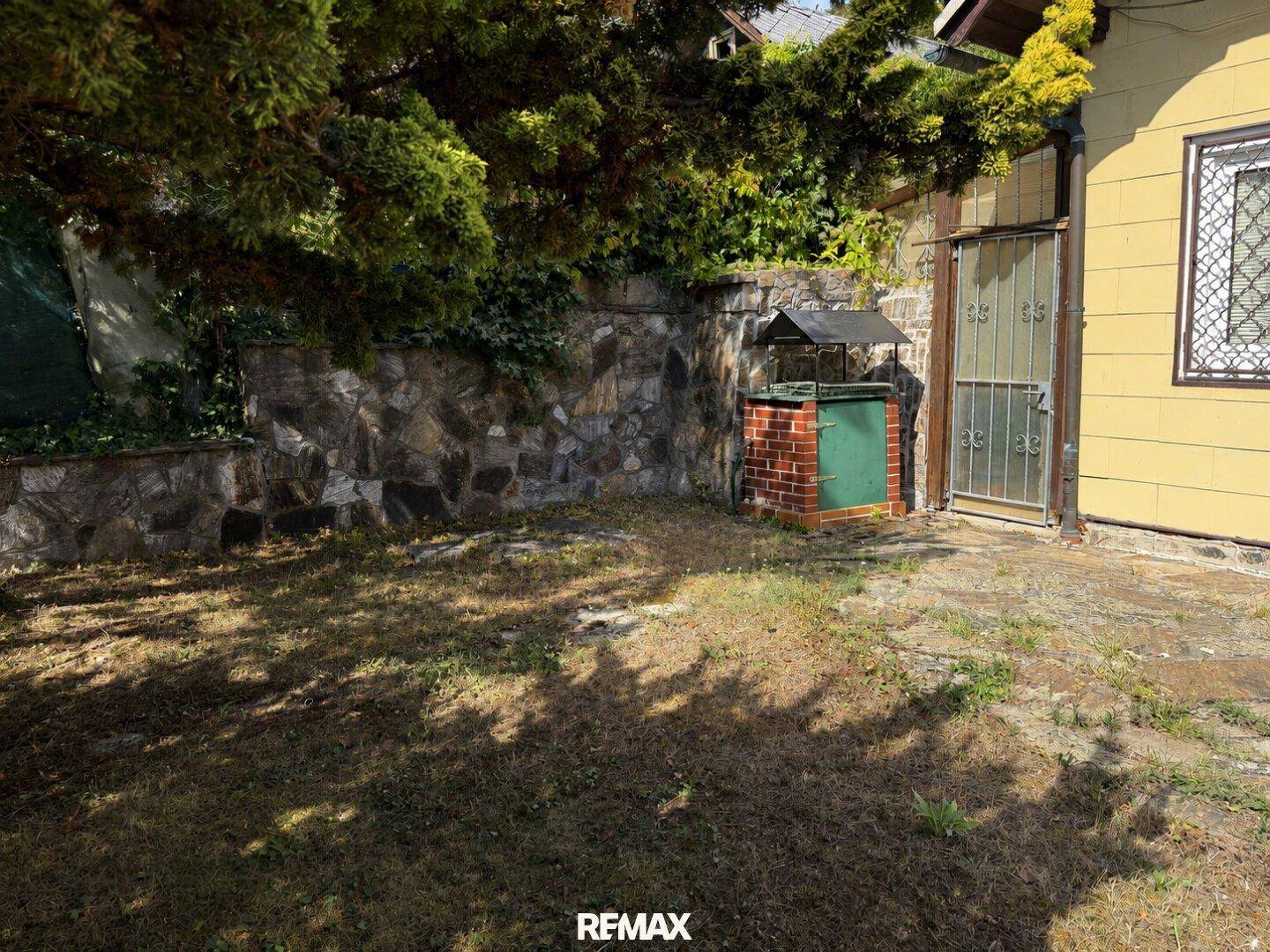 Kleiner Gartenbereich mit Rasen, einer Steinmauer und einem gemauerten Grillplatz neben dem Haus.