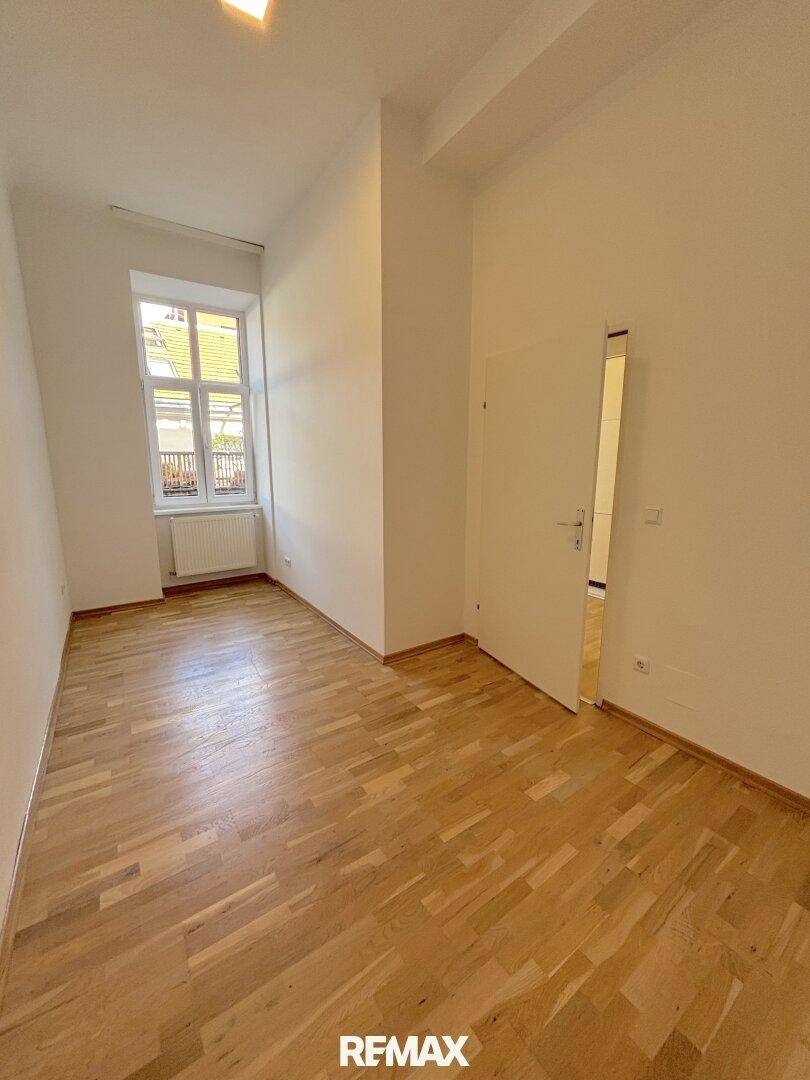 Geräumiges Zimmer mit Holzparkettboden und einem Fenster, das Tageslicht hereinlässt.