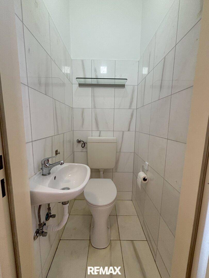 Kleines separates WC mit Toilette, Waschbecken und weißen Wandfliesen.