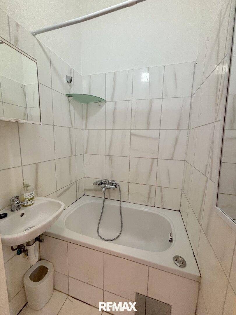 Gefliestes Badezimmer mit Badewanne, Waschbecken und einem kleinen Spiegel.