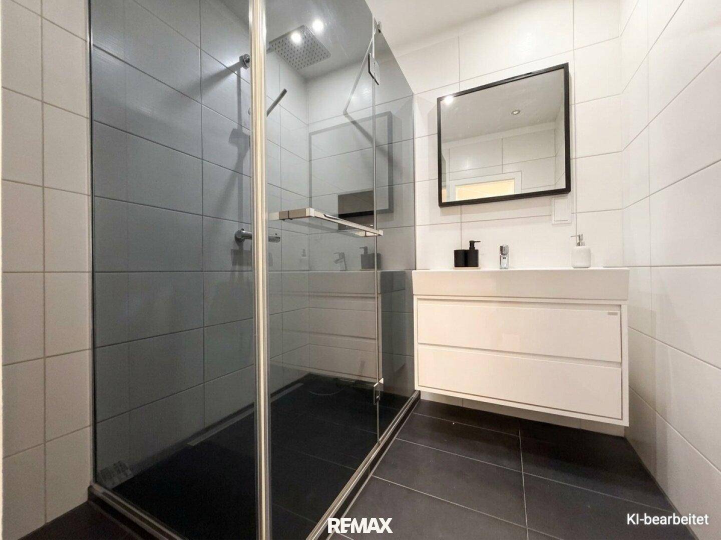 Modernes Badezimmer mit großer begehbarer Dusche, weißen Fliesen und dunklem Boden.