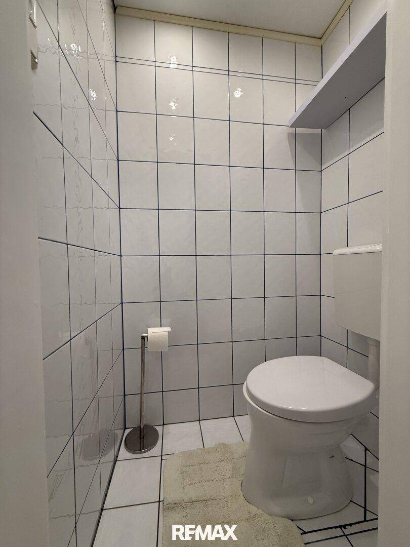 Kleines, hell gefliestes WC mit Toilette und einfacher Ausstattung.