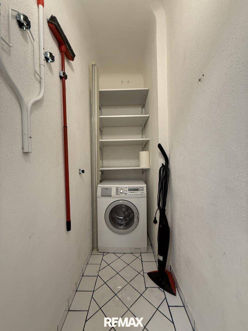 Praktischer Hauswirtschaftsraum mit Waschmaschine, Regalen und Stauraum für Reinigungsgeräte.