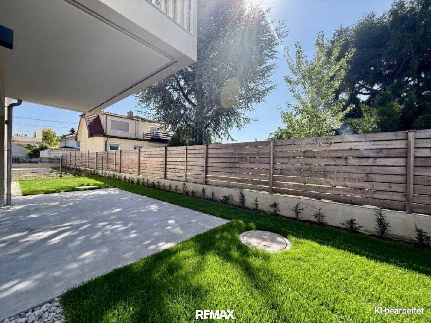 Sonnige Terrasse mit Rasenfläche und modernem Holzzaun, ideal für Entspannung im Freien.