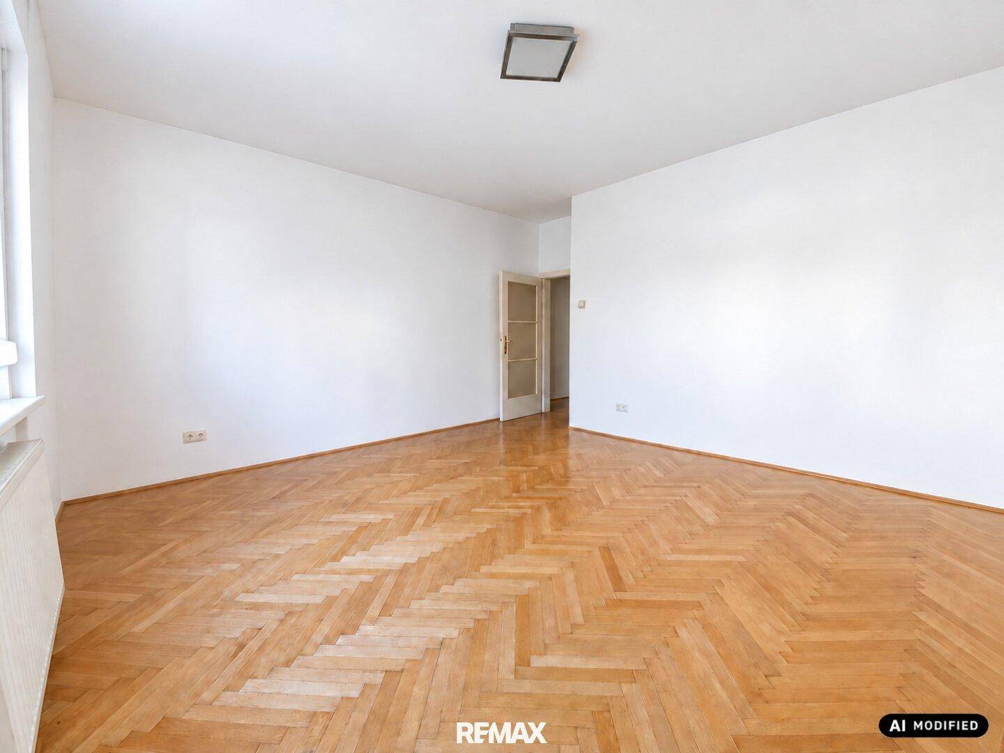 Geräumiges, leeres Zimmer mit klassischem Fischgrätparkett und einer Tür zu einem weiteren Raum.