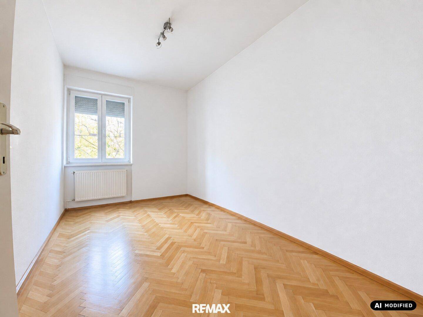 Unmöbliertes Zimmer mit Fischgrätparkett, weiß gestrichenen Wänden und einem Fenster mit Heizkörper.