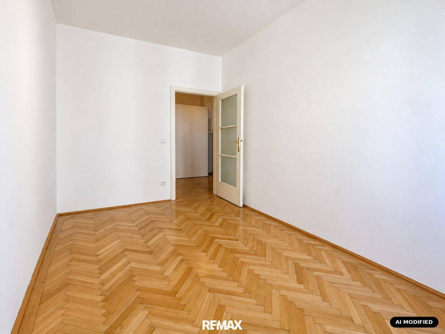 Leeres Zimmer mit hellem Fischgrätparkett und einer Tür mit Glaseinsatz.