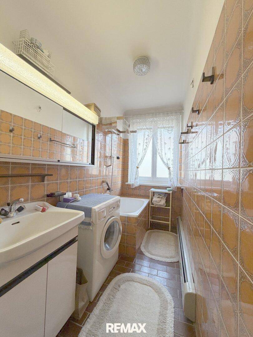 Badezimmer mit orangefarbenen Fliesen, Badewanne, Waschmaschine und einem Fenster für Tageslicht.