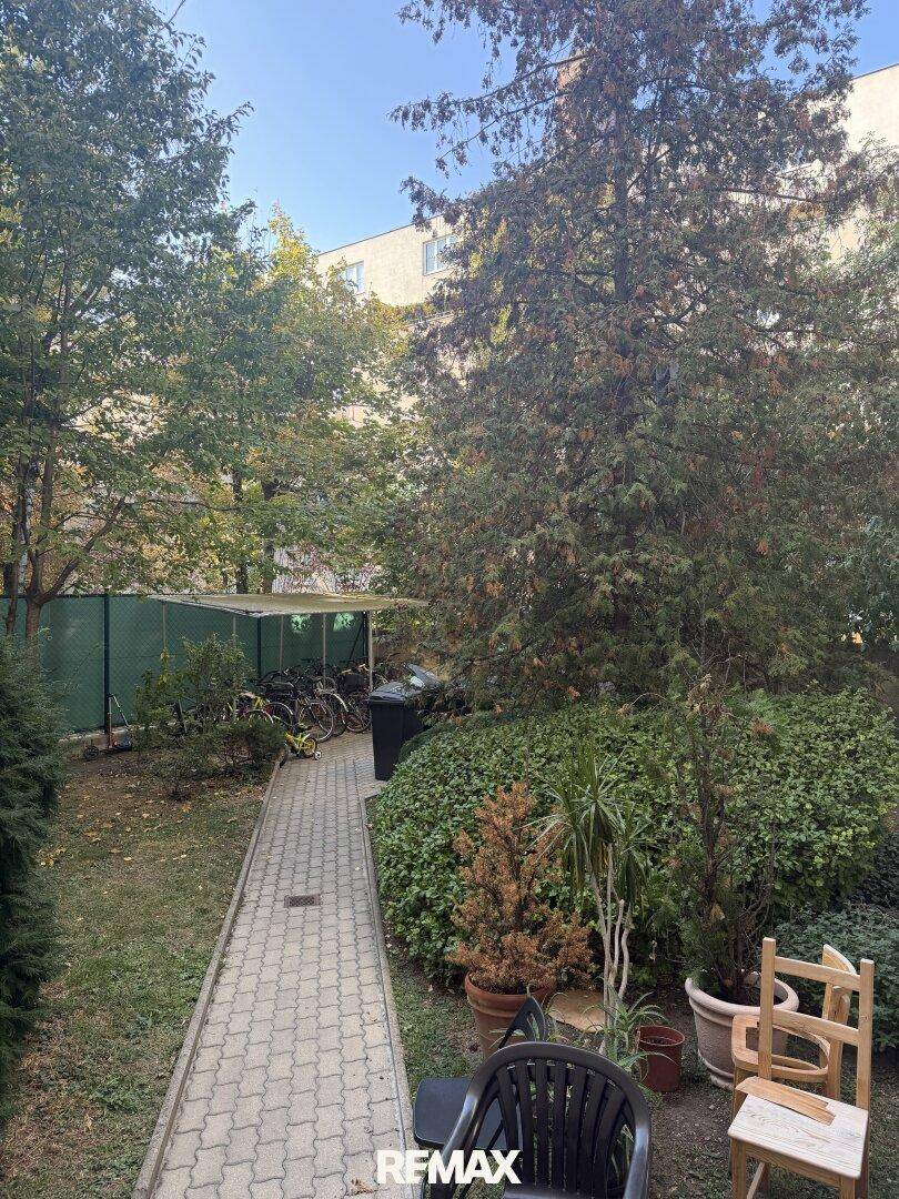 Gepflegter Gemeinschaftsgarten mit Gehwegen, Bäumen und einem überdachten Fahrradabstellplatz.