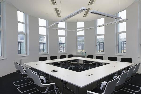 Moderner Konferenzraum mit U-förmigem Tisch, vielen Fenstern und minimalistischem Design für Besprechungen.