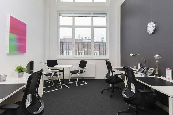 Helles Einzelbüro mit dunkler Akzentwand, großem Fenster und mehreren Arbeitsplätzen für konzentriertes Arbeiten.