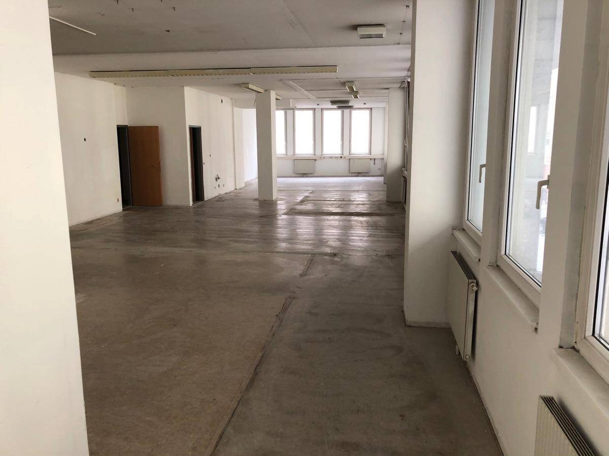 Langer, unmöblierter Bürobereich mit vielen Fenstern und einem Betonboden, der auf den Ausbau wartet.