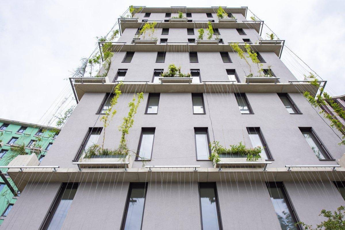 Fassadenansicht eines modernen Gebäudes mit vertikalen Grünpflanzen und großen Fenstern unter bewölktem Himmel.