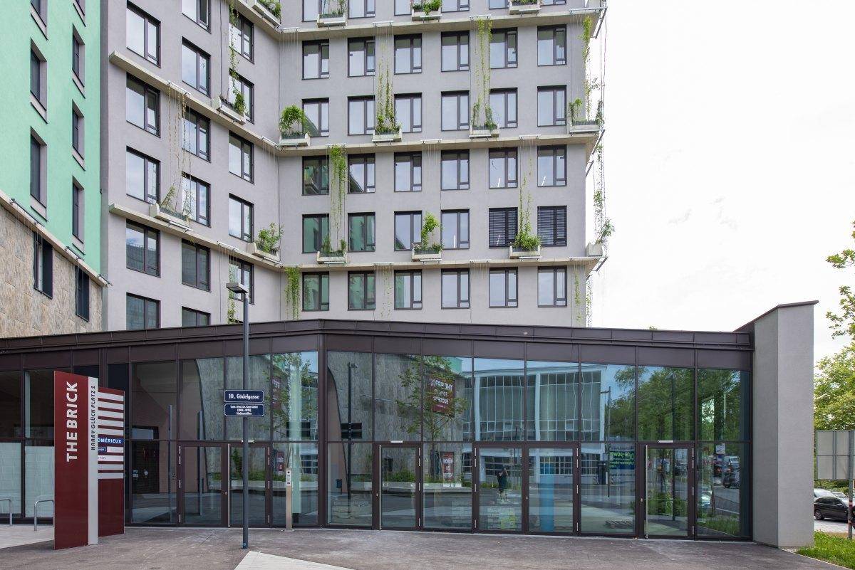 Moderner Eingangsbereich eines Gebäudes mit großer Glasfassade und deutlicher Beschilderung, einladend gestaltet.