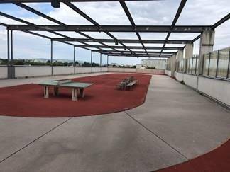 Große Dachterrasse mit Tischtennisplatte und Sitzgelegenheiten, umgeben von einer Metallkonstruktion unter offenem Himmel.