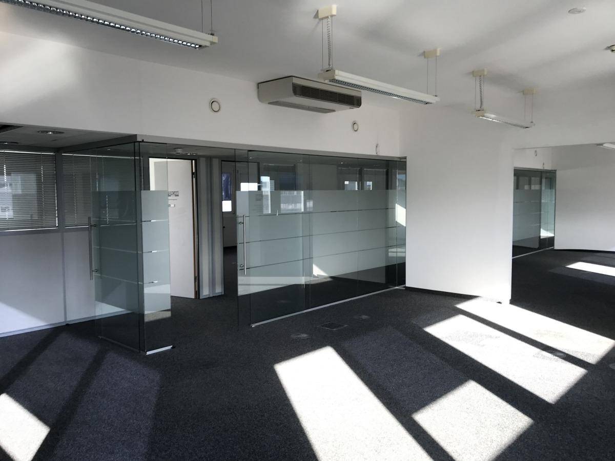 Geräumiger Büroraum mit Teppichboden, Glasabtrennungen und viel natürlichem Licht durch die Fenster.