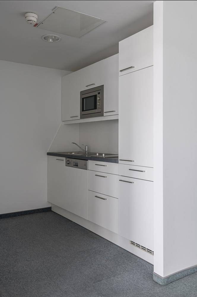 Kompakte, moderne Küchenzeile mit weißen Schränken, Spüle und integrierter Mikrowelle in einem Bürogebäude.