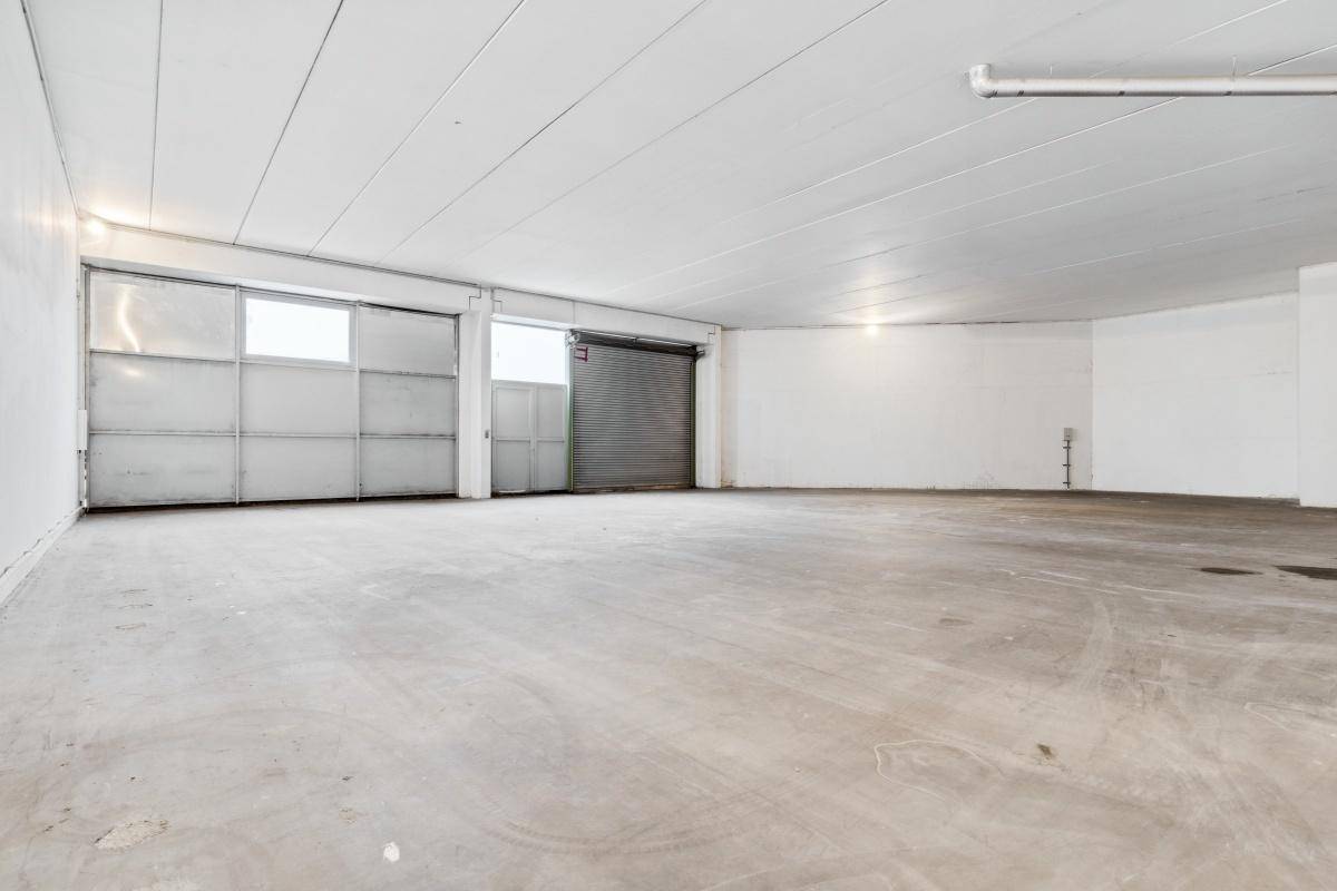 Leere Lagerhalle mit Betonboden, Rolltor und hohen Decken, ideal für Logistik oder Produktion.