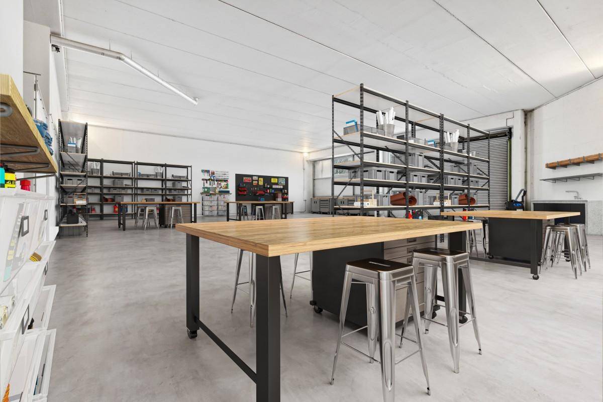 Heller Werkstattbereich mit robusten Holzarbeitsplatten, Metallregalen und Betonboden für kreative oder handwerkliche Arbeiten.