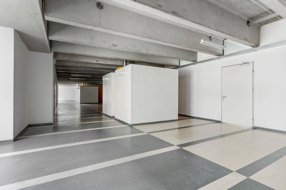 Tiefgaragenbereich mit Betonstützen, Schachbrettmuster auf dem Boden und Zugangstüren, ideal für Fahrzeuge.