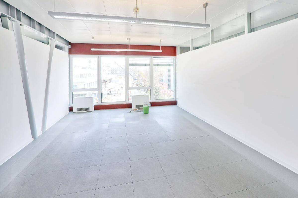 Leerer Büroraum mit großen Fenstern, Fliesenboden und weißen Trennwänden, bereit zur Einrichtung.