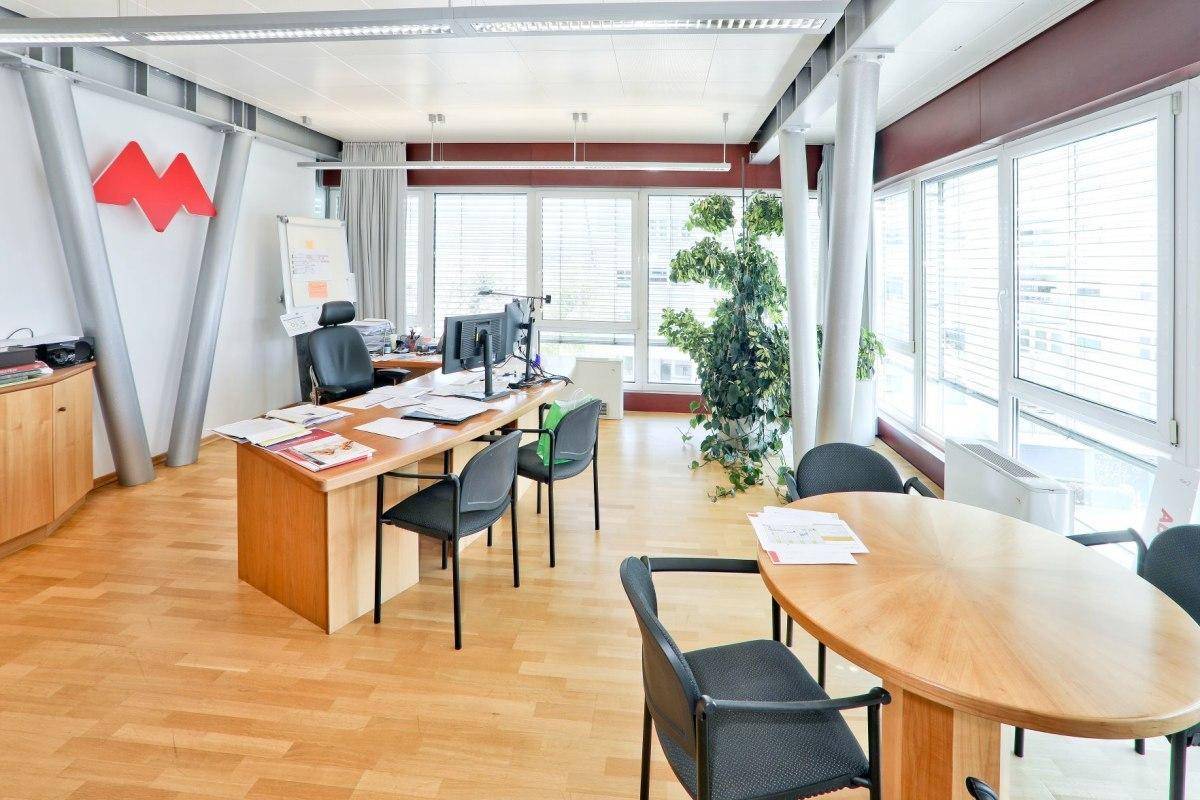 Helles Einzelbüro oder Besprechungsraum mit Holzboden, großen Fenstern und Holztischen, gut beleuchtet.