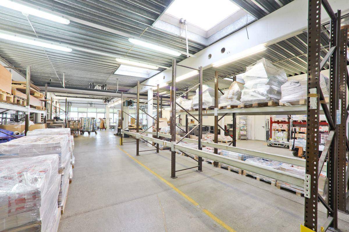 Langer Gang in einem Lagerraum mit hohen Regalen, Oberlichtern und verpackten Produkten, bereit zum Versand.