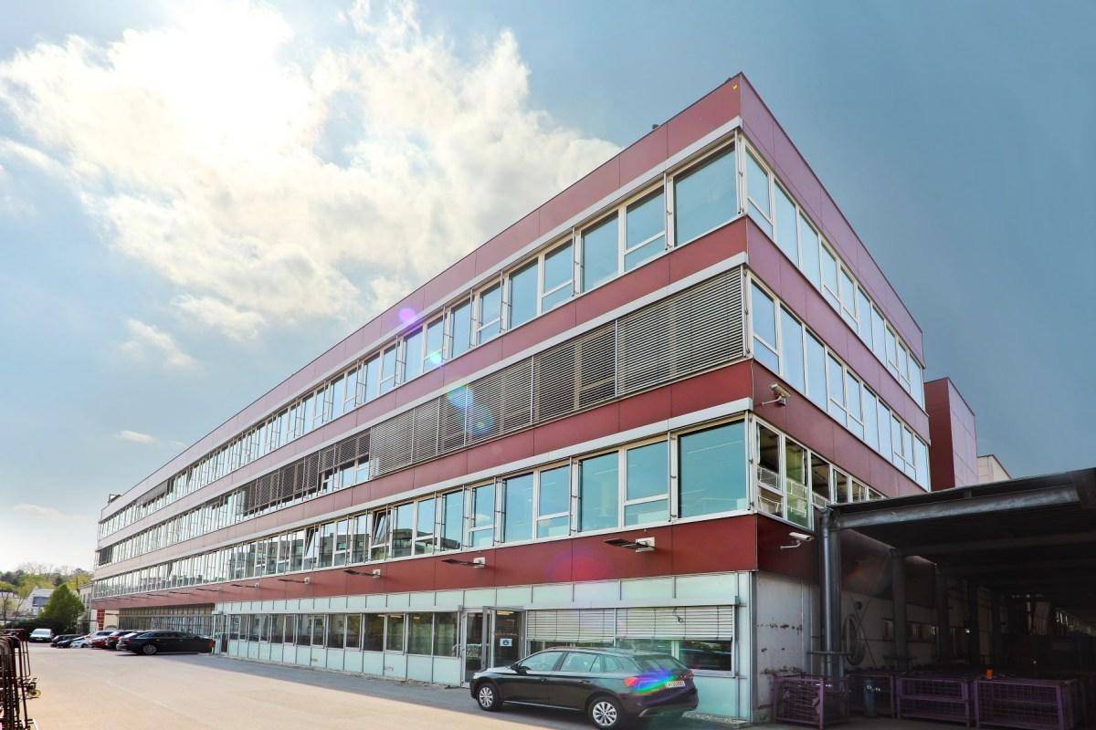 Modernes Geschäftsgebäude mit roter Fassade, vielen Fenstern und einem Ladebereich unter bewölktem Himmel.