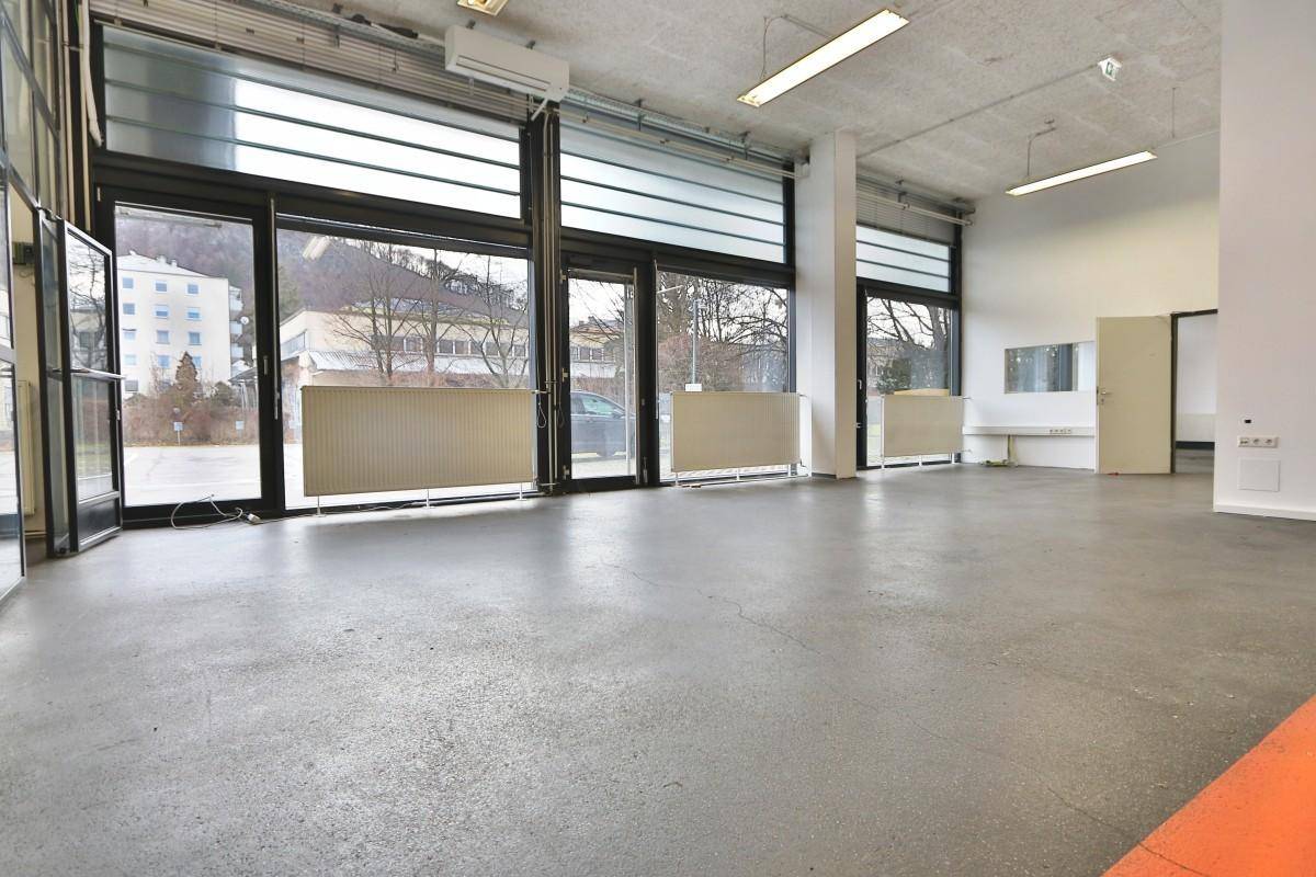 Großer, heller Raum mit Betonboden, hohen Fenstern und Blick auf die Straße, ideal für gewerbliche Nutzung.