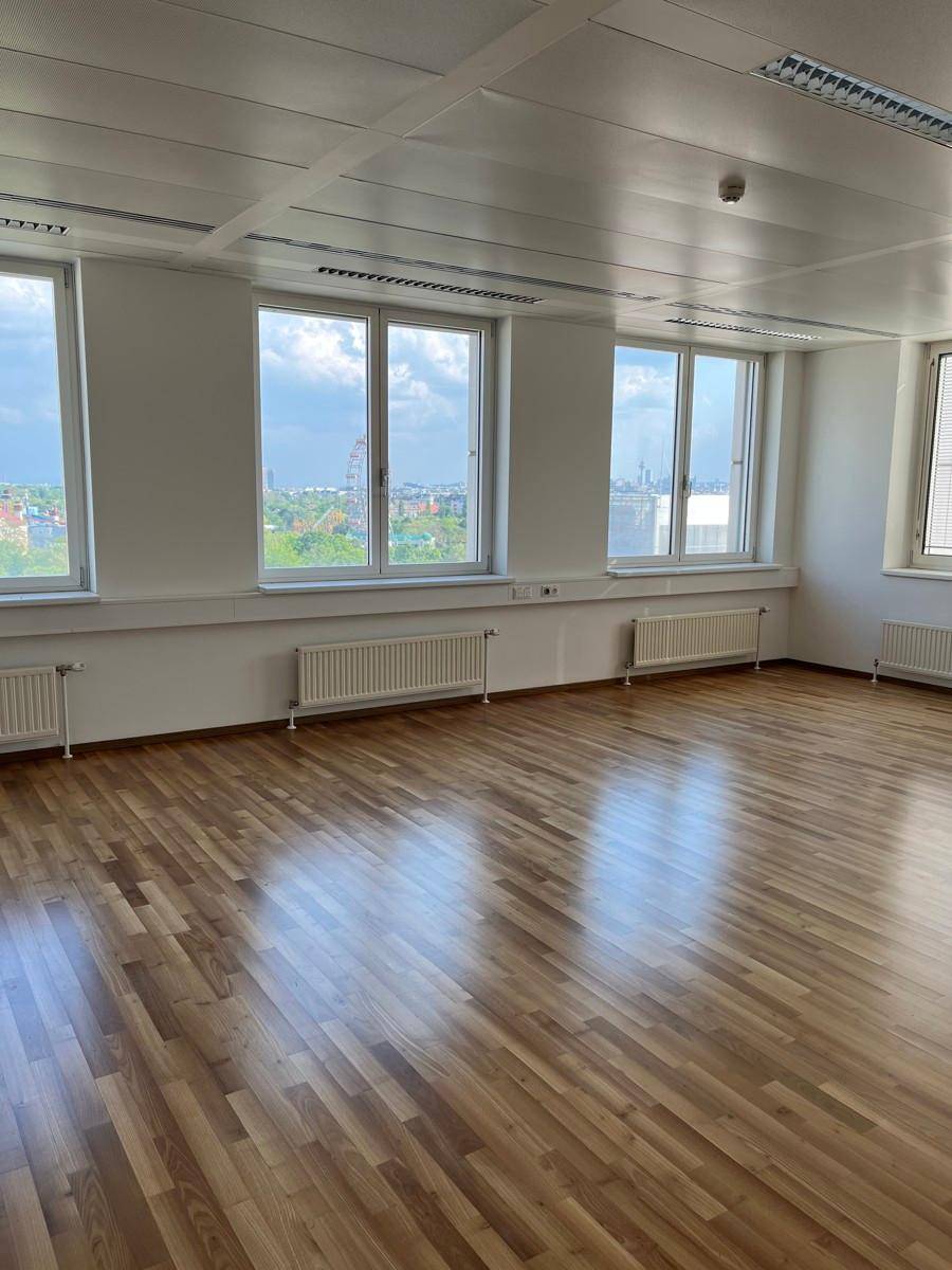Heller Büroraum mit hellem Holzboden, großen Fenstern und Heizkörpern, bietet eine weite Aussicht.