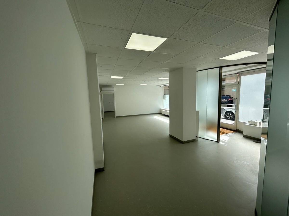 Offener Bürobereich mit Säulen, Vinylboden und Blick auf den Eingangsbereich mit großer Glasfront.