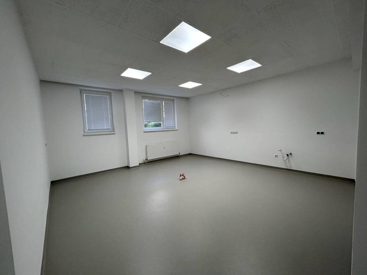Heller Büroraum mit zwei Fenstern, Heizkörper und Wandanschlüssen.