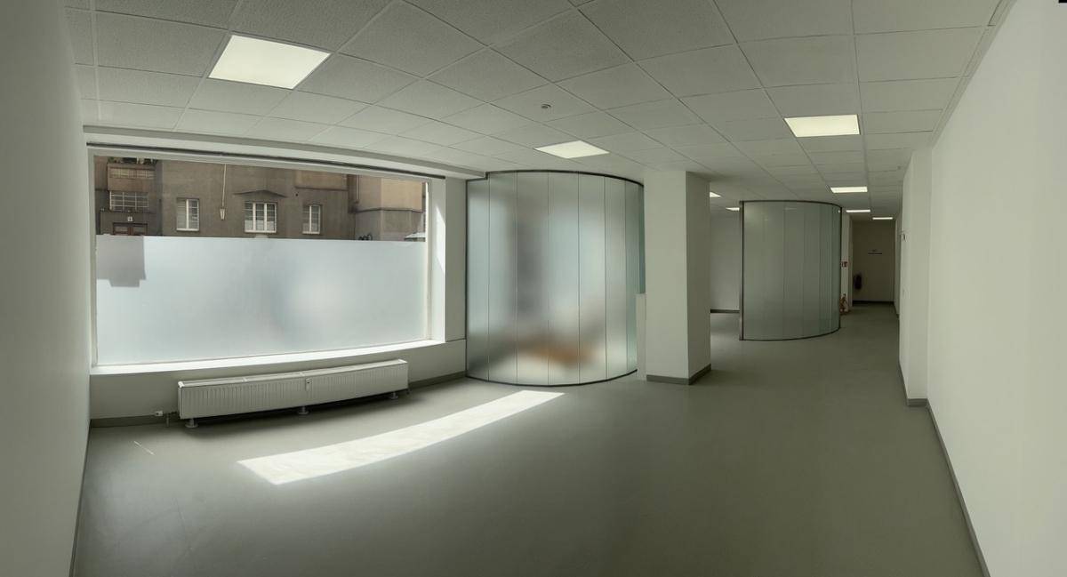 Weitläufiger Bürobereich mit großen Fenstern, hellgrauem Boden und geschwungenen Glaswänden als Raumteiler.