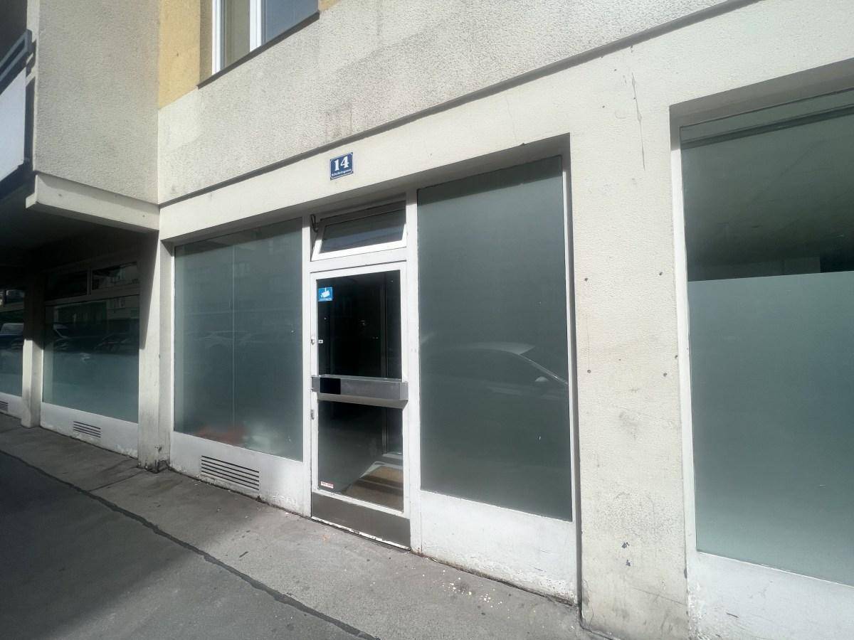 Nahaufnahme der Geschäftsfassade mit Eingangstür und großen, undurchsichtigen Schaufenstern an einem sonnigen Tag.