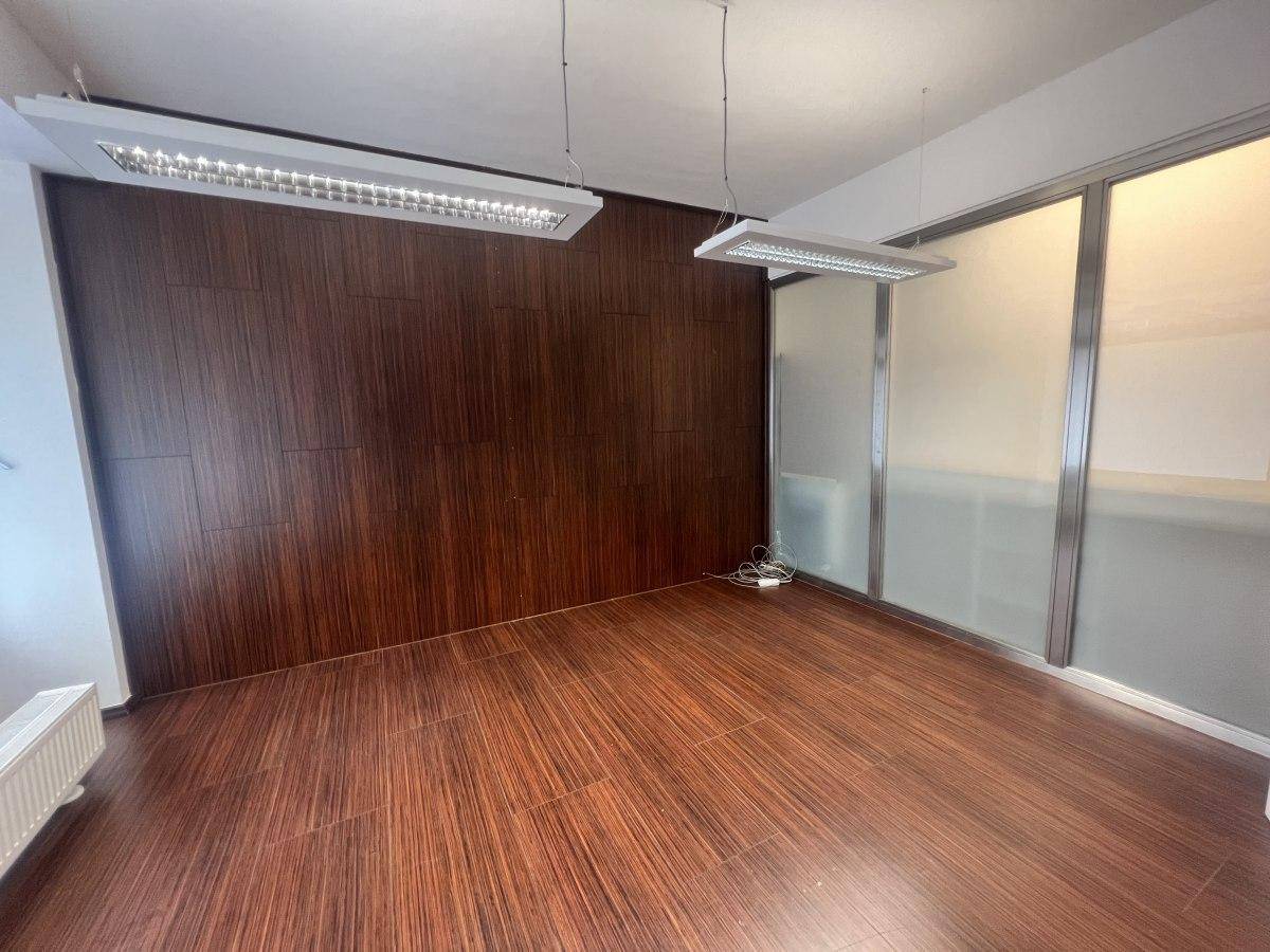 Büroraum mit dunklem Holzboden, einer Akzentwand aus Holzpaneelen und modernen Deckenleuchten.