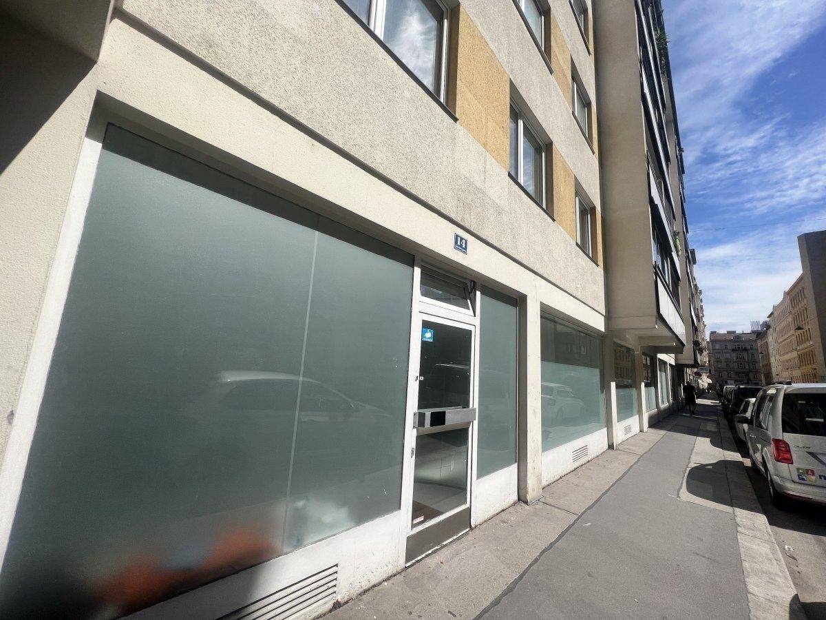 Ansicht der Geschäftsfassade eines Mehrfamilienhauses mit großen Schaufenstern und Eingangstür an einer belebten Straße.