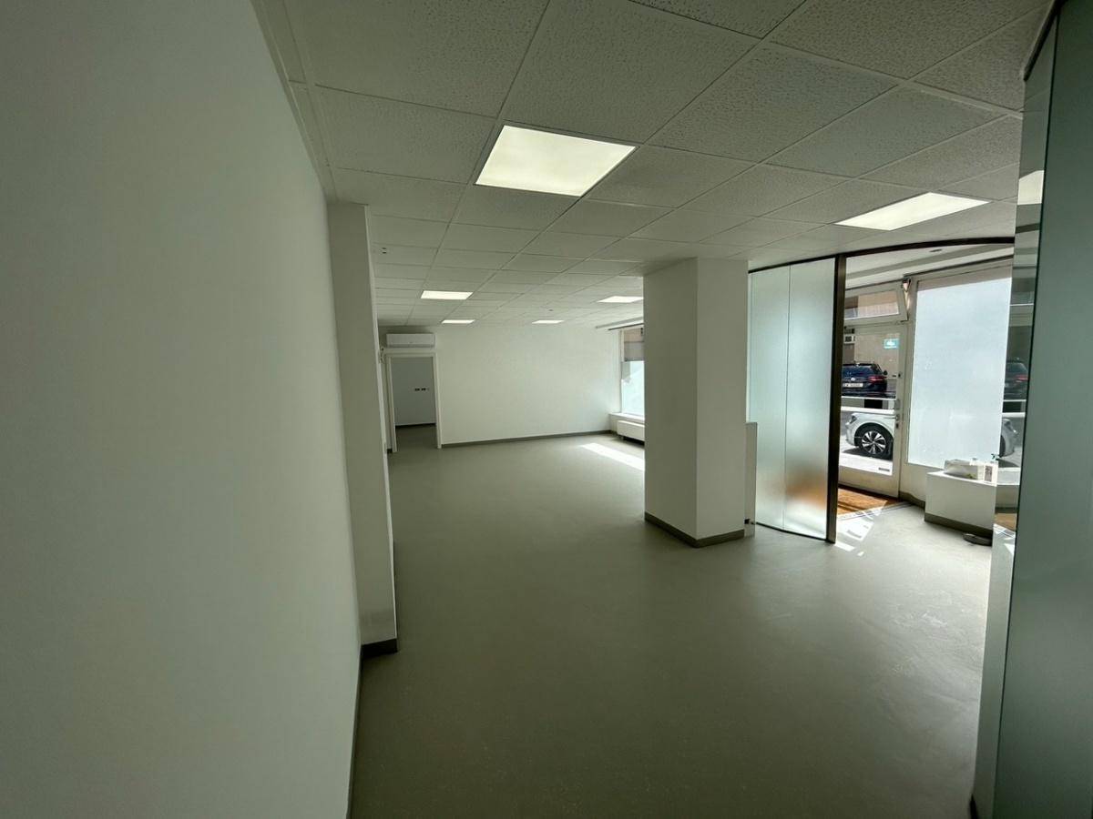 Offener Bürobereich mit hellem Boden, weißen Wänden und einer Glasfront zum Eingangsbereich.
