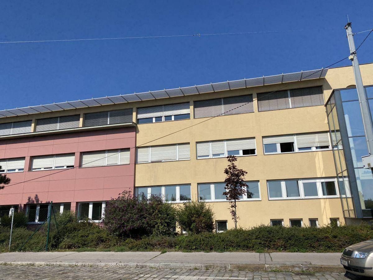 Seitenansicht eines Gebäudes mit gelber und rosafarbener Fassade, vielen Fenstern und Sonnenschutz.